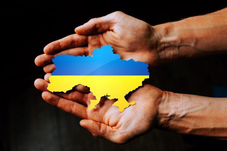 hands holding cutout of the shape of Ukraine, the cutout has blue and yellow, colors of Ukrainian flag