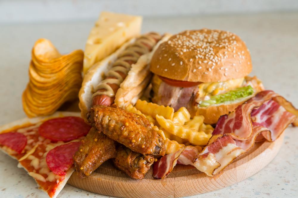 Round wooden platter with French fries, pizza, hot dogs, and a hamburger on top, some of the top ten favorite American foods